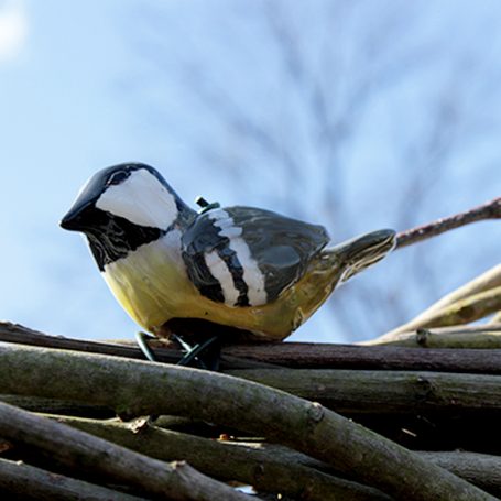 A figurine of a bird perched on branches against a blue sky.