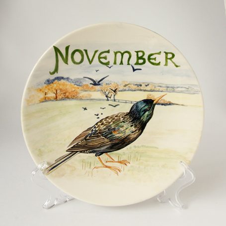 A decorative plate featuring a bird and the word "November" with a landscape background.