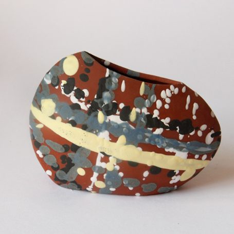 Abstract ceramic vase with a textured surface in earthy colours and bold patterns.