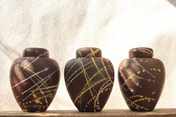 Three decorative jars with brown surfaces and abstract yellow and white patterns.