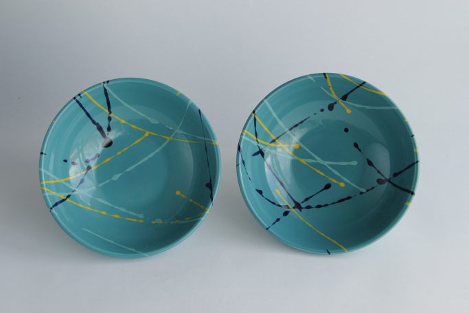 Two turquoise plates with abstract black and yellow designs.