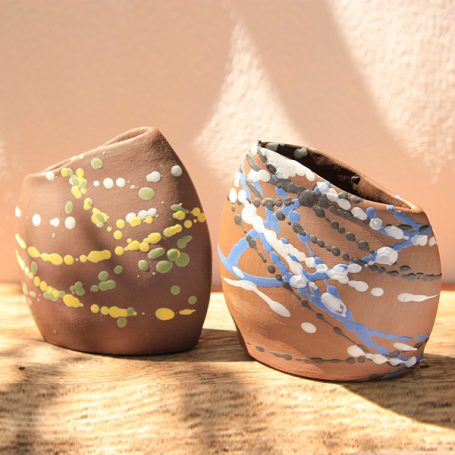 Two abstract clay vases with colourful patterns against a soft background.