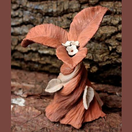 A whimsical figure made of clay with large leaf-like petals and a clay face.