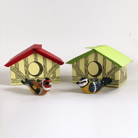 Colourful bird figurines in front of two miniature birdhouses with red and green roofs.