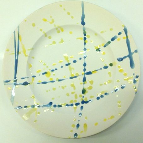 White plate with abstract blue and yellow paint splashes and lines.