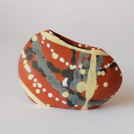 Clay vase with a smooth, irregular shape, featuring abstract red and yellow patterns.