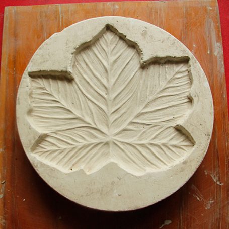 Relief sculpture of a large leaf on a circular stone surface.