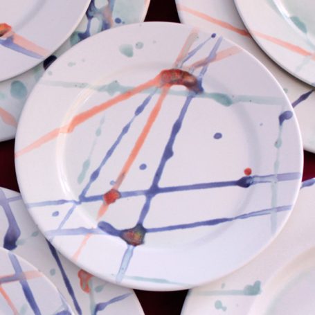 White plate featuring an abstract pattern of blue, orange, and green splashes and lines.