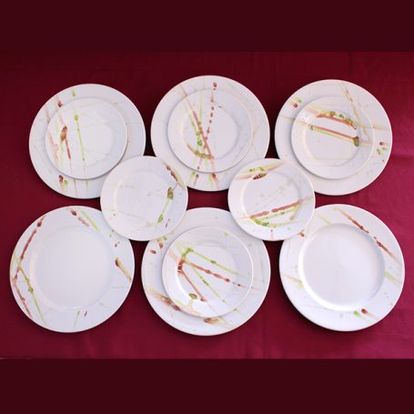 A set of white plates with colourful, abstract designs arranged on a red background.