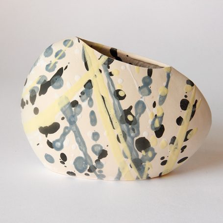 Abstract ceramic vase with splashes of blue, yellow, and black on a soft white surface.