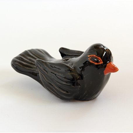 A small black ceramic bird with a bright orange beak and detailed feather texture.