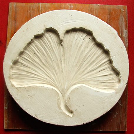 Relief sculpture of a ginkgo leaf on a circular base.