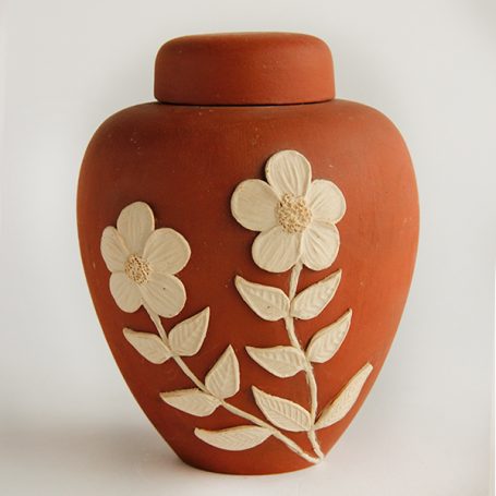 Terracotta urn with white floral relief design and a lid.