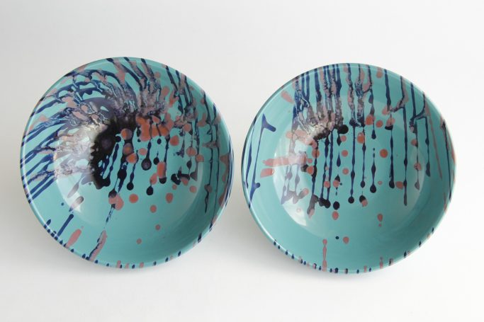 Two turquoise bowls with abstract splatter patterns in blue, red, and black.