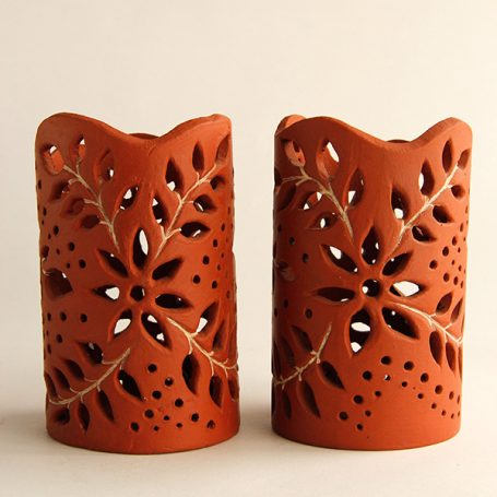 Two terracotta candle holders with floral cut-out designs.