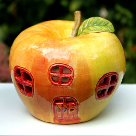 A ceramic apple-shaped house with red windows and a green leaf on top.