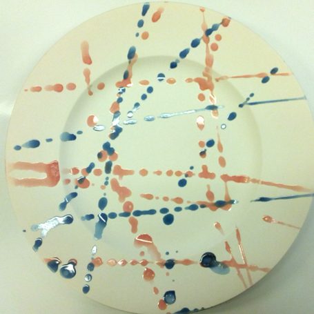 A white plate with abstract blue and coral splashes and lines.