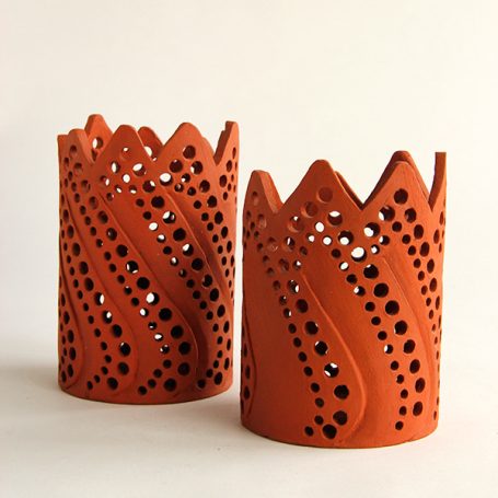 Two decorative terracotta candle holders with intricate cut-out patterns.