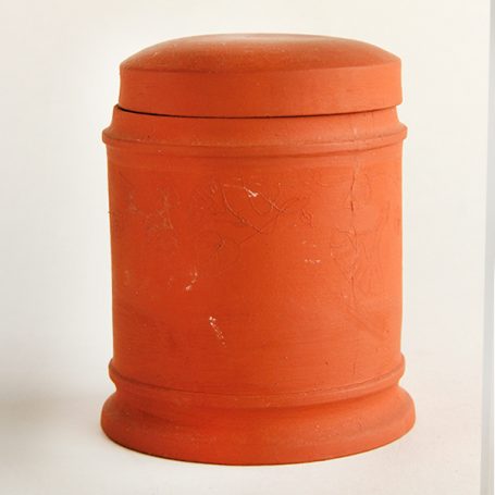 Terracotta cylindrical container with a rounded lid and a smooth surface.