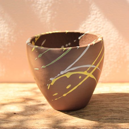 Brown ceramic pot with yellow and white abstract lines on a wooden surface.