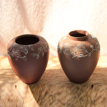 Two decorative clay vases with floral engravings, one taller than the other.
