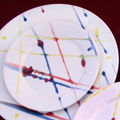White plates with colourful paint splatter in red, yellow, and blue patterns.