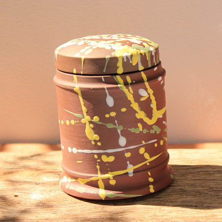 A brown jar with colourful paint splatters on its surface.