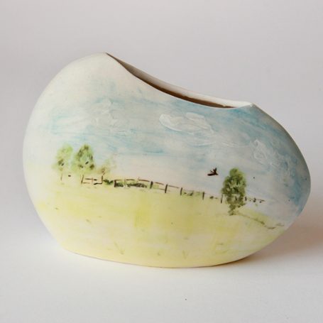 Ceramic vase with a painted landscape featuring trees and a blue sky.