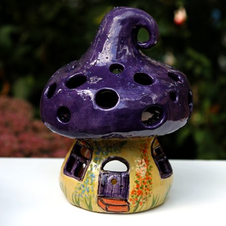 Whimsical ceramic mushroom house with purple top and colourful door and flower details.