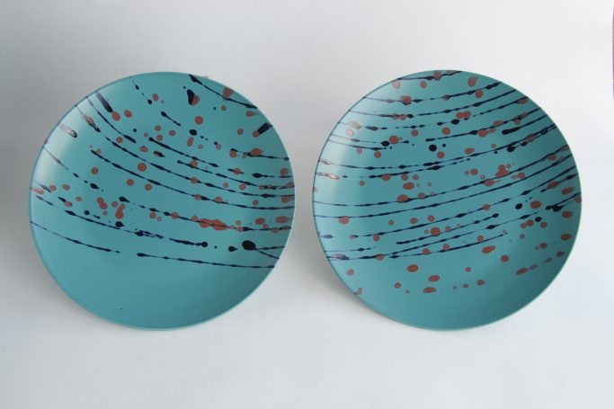 Two turquoise plates with abstract red and black splatter patterns.