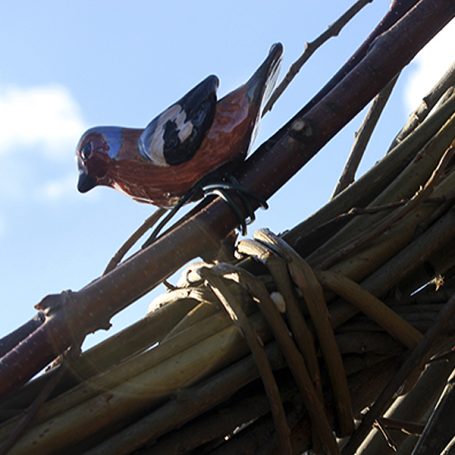 A decorative bird figurine perched on a woven structure against a blue sky.