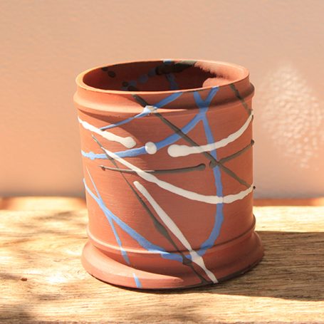 Ceramic pot with abstract blue, white, and black markings on a terracotta background.
