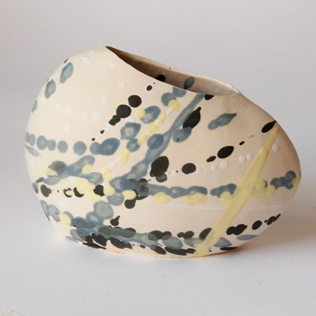 Abstract ceramic vase with a shimmer of blue, black, and yellow dots on a white background.