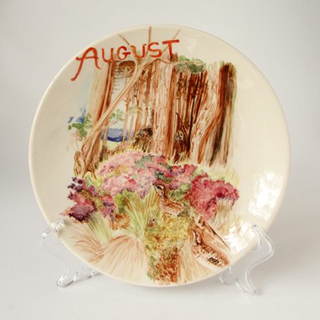 A decorative plate featuring a floral scene and the name "August" written in red.
