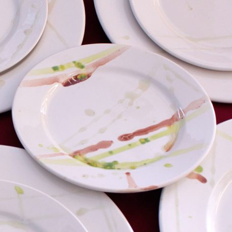 A collection of white plates with abstract, colourful splashes and streaks.